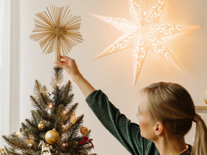 A woman places a decorative straw star on top of the FairyTrees FT01 artificial Christmas tree.