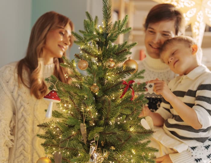 Mom, dad, and son share a quiet moment close to the glowing artificial Christmas tree FairyTrees FT05 in a warm, festive scene.