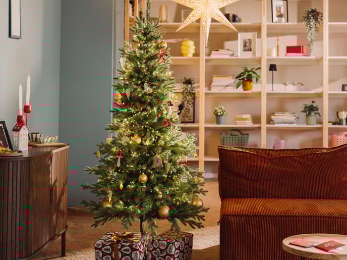 Artificial Nordmann fir FairyTrees FT05 stands beautifully decorated in the living room of a small apartment on a winter evening.