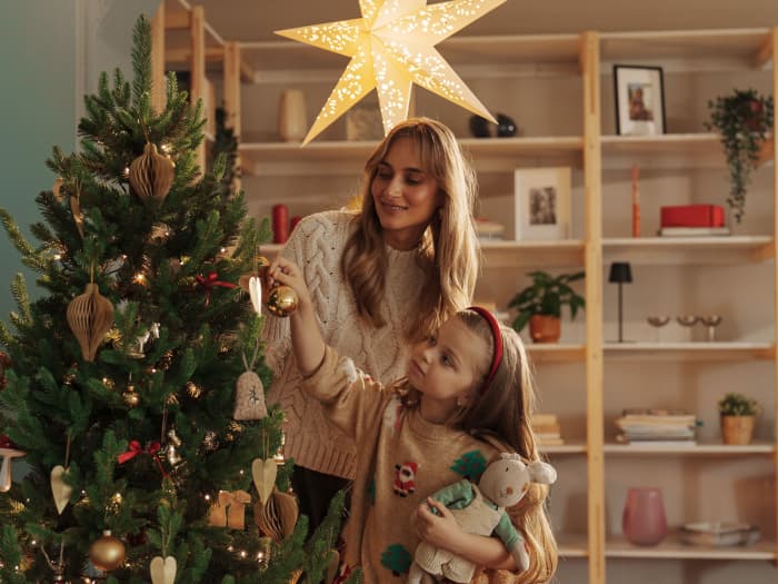 Mother and daughter decorate the FairyTrees FT32 artificial Christmas tree with golden baubles in a cozy living room