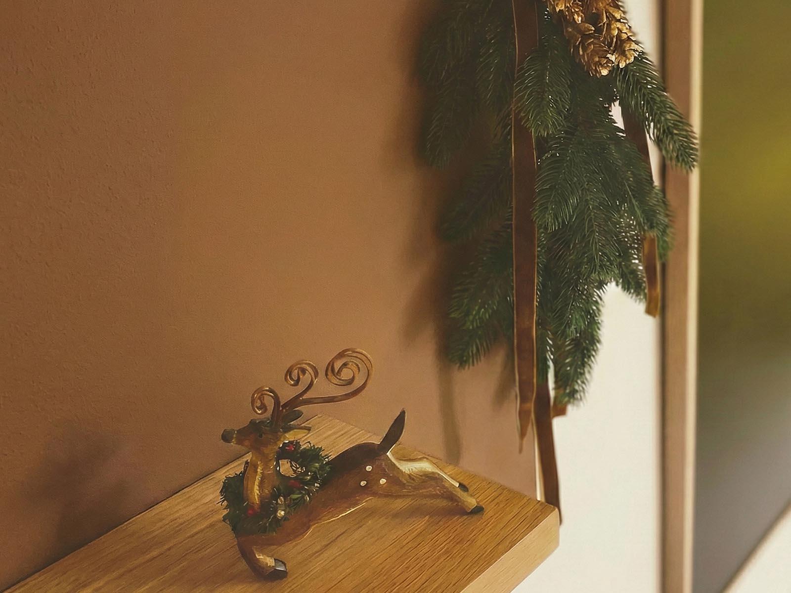 In the hallway, there is a FairyTrees artificial Christmas tree branch and pine cone decoration hanging on the wall, and a reindeer figurine stands on the countertop.