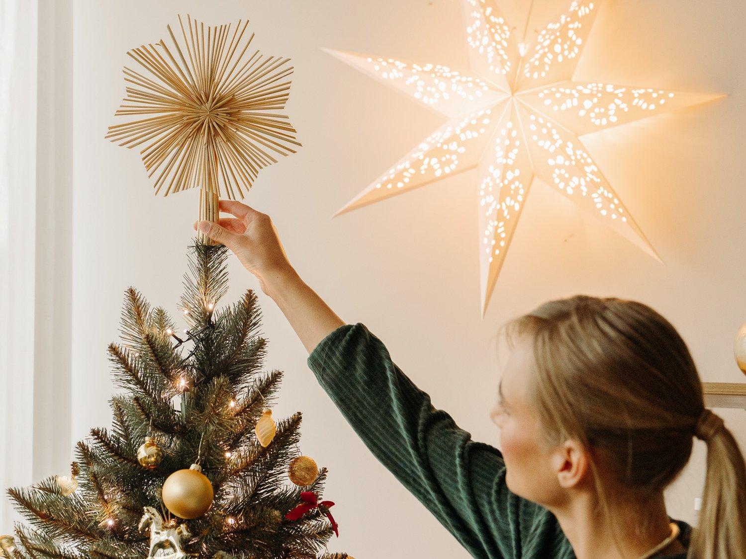 A woman places a decorative straw star on top of the FairyTrees FT01 artificial Christmas tree.