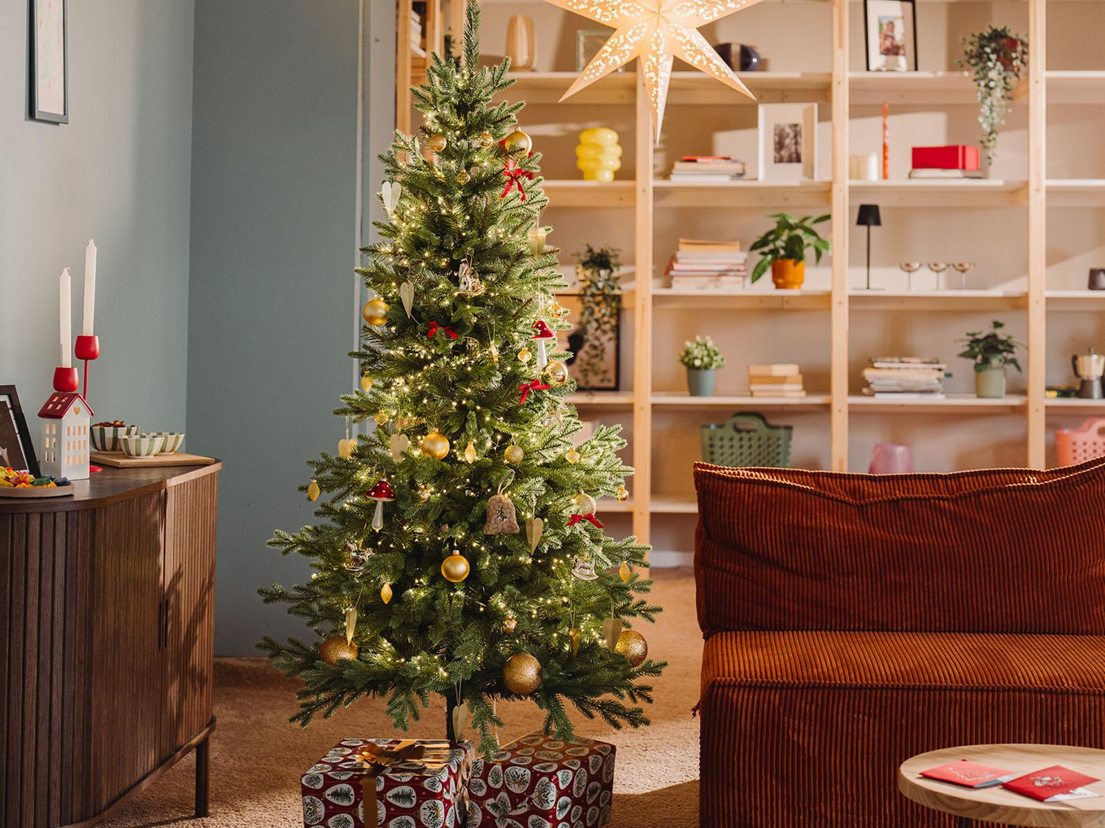 Artificial Nordmann fir FairyTrees FT05 stands beautifully decorated in the living room of a small apartment on a winter evening.