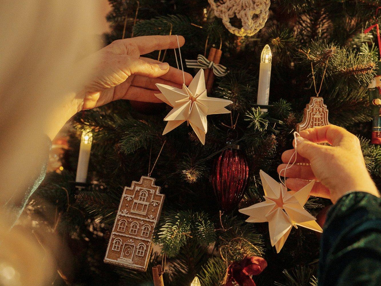 A woman’s hands hang paper stars on a decorated FairyTrees FT29 artificial Christmas tree.