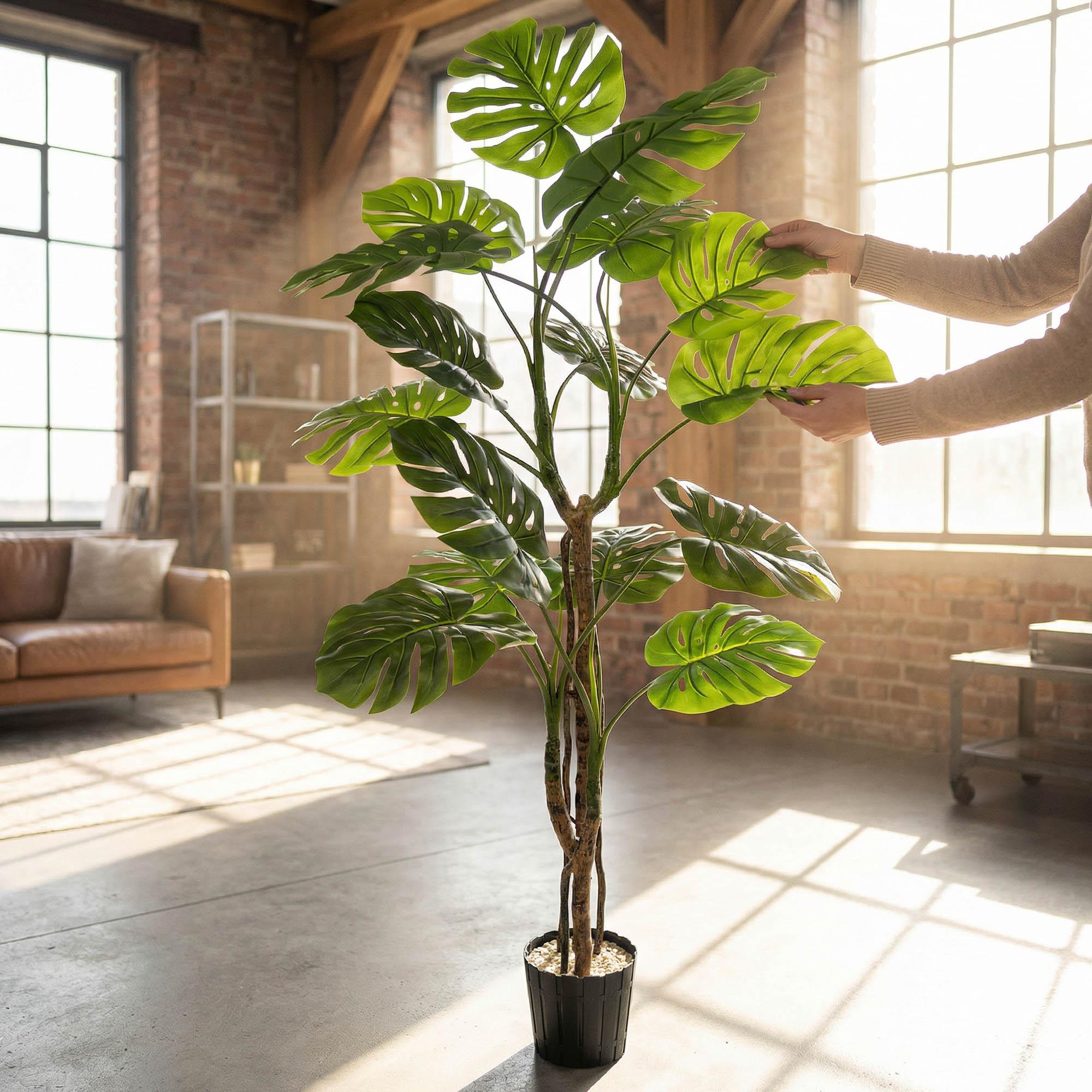 Hands adjust the leaves of the 160 cm FairyTrees artificial monstera on a trunk, highlighting their natural appearance and flexibility.