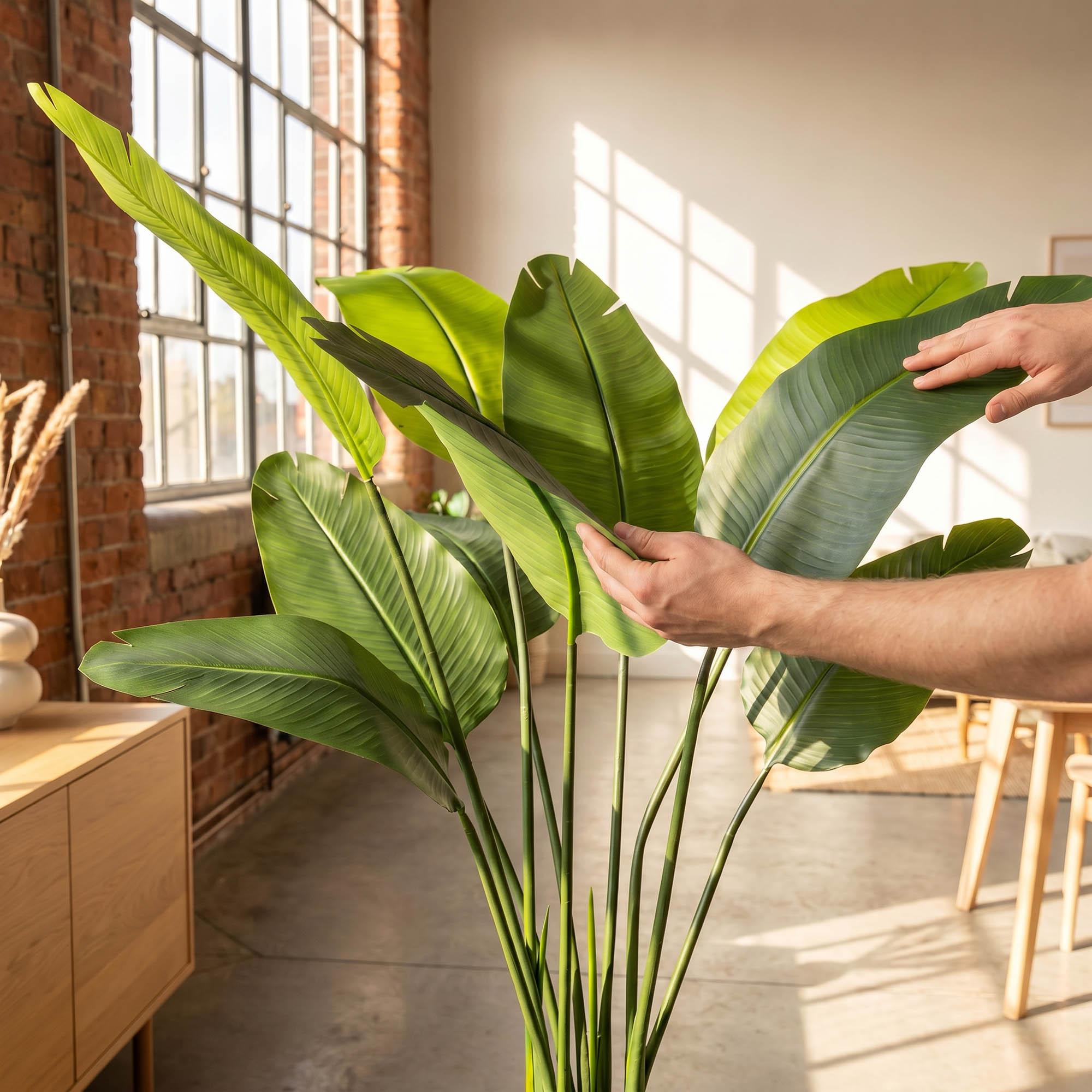 Hands adjust the leaves of the 160 cm FairyTrees artificial monstera on a trunk, highlighting their natural appearance and flexibility.
